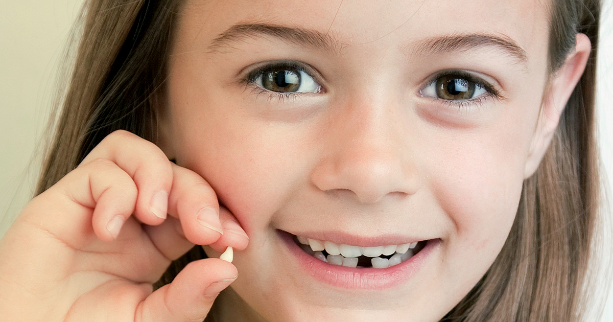 young girl smiling and holding up a lost tooth