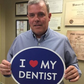 middle-aged male patient holding blue sign that says I love my dentist 